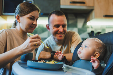 The first pure baby food. Mother gives a spoonful of vegetables in a chair for feeding at home....