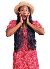 Young african american woman wearing summer hat afraid and shocked, surprise and amazed expression with hands on face