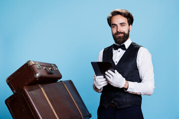 Hotel concierge checks online reservations on gadget, standing next to suitcases for safekeeping....