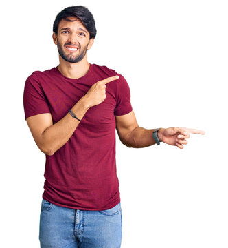 Handsome hispanic man wearing casual clothes pointing aside worried and nervous with both hands, concerned and surprised expression