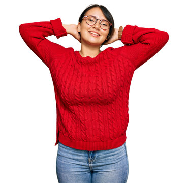 Young beautiful hispanic woman with short hair wearing casual sweater and glasses relaxing and stretching, arms and hands behind head and neck smiling happy
