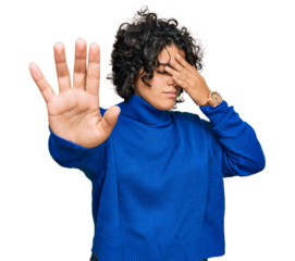 Young hispanic woman with curly hair wearing turtleneck sweater covering eyes with hands and doing stop gesture with sad and fear expression. embarrassed and negative concept.
