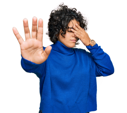 Young hispanic woman with curly hair wearing turtleneck sweater covering eyes with hands and doing stop gesture with sad and fear expression. embarrassed and negative concept.
