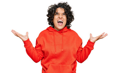 Young hispanic woman with curly hair wearing casual sweatshirt crazy and mad shouting and yelling...