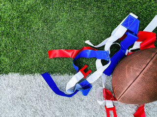 Flag Football Equipment on Green Turf. White belts with red and blue flags used for playing flag football. A football lays to the side. Set against the white and green turf of a football field.