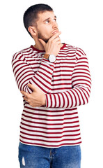 Young handsome man wearing striped sweater with hand on chin thinking about question, pensive expression. smiling with thoughtful face. doubt concept.