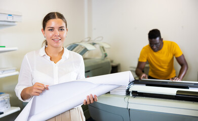Happy young female specialist in white shirt holding whatman in a roll in the typography