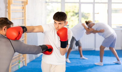 Man and young guy at group boxing lesson are learning new technique of body blowing, mam is...