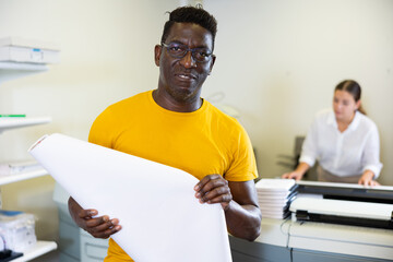 Portrait of friendly male employee of printing house with a stack of notebooks in her hands