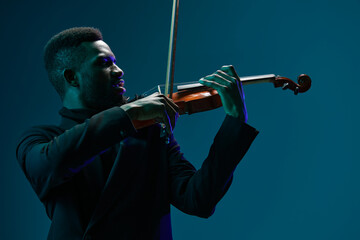 Elegant man in black suit playing violin on vibrant blue background with passion and skill