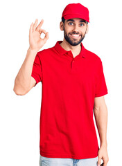 Young handsome man with beard wearing delivery uniform smiling positive doing ok sign with hand and fingers. successful expression.