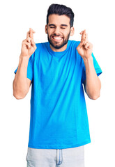 Fototapeta premium Young handsome man with beard wearing casual t-shirt gesturing finger crossed smiling with hope and eyes closed. luck and superstitious concept.