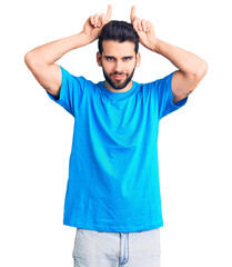 Fototapeta premium Young handsome man with beard wearing casual t-shirt doing funny gesture with finger over head as bull horns