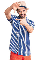 Young handsome man with beard wearing summer hat and striped shirt smiling making frame with hands and fingers with happy face. creativity and photography concept.