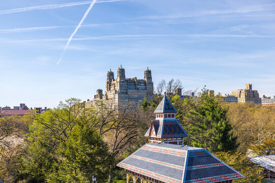 Beautiful view of Belvedere Castle in Central Park, New York City, with contrasting modern skyscrapers in the background and striking jet trails in the blue sky.