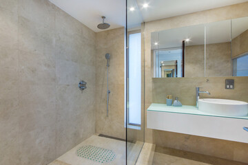 Modern design of the hotel bathroom with beige tiles. A shower stall and a large mirror over the...