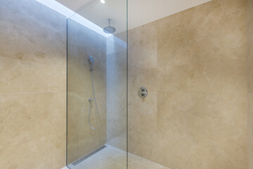Shower cabin in the hotel with a glass partition and beige tile walls.