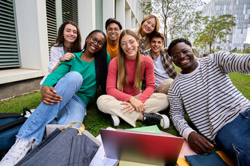 Portrait of a large group multiracial friends sitting posing smiling with laptop and workbooks...