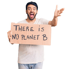 Young hispanic man holding there is no planet b banner celebrating victory with happy smile and winner expression with raised hands