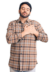 Young hispanic man wearing casual clothes smiling with hands on chest with closed eyes and grateful gesture on face. health concept.