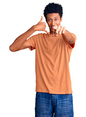 Young african american man wearing casual clothes smiling doing talking on the telephone gesture and pointing to you. call me.