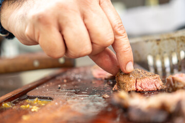 Man grabbing a pieces of freshly cooked beef on barbecue