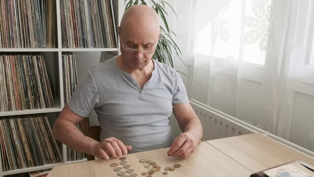poor pensioner, Senior man with reading glasses lays out euro cent coins on wooden table, counts meager cash money on table, illustrating harsh reality of life in poverty