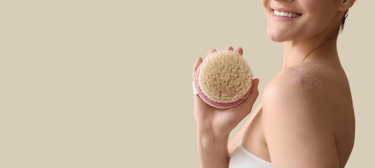 Young woman scrubbing body with massage brush on light background with space for text