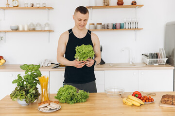 Athletic muscular man holding salad leaves and preparing food in the kitchen at home