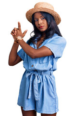 Young indian girl wearing summer hat holding symbolic gun with hand gesture, playing killing shooting weapons, angry face