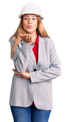 Beautiful young woman wearing architect hardhat looking at the camera blowing a kiss with hand on air being lovely and sexy. love expression.