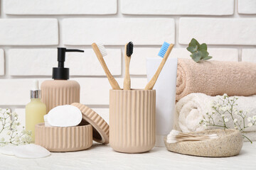 Set of bath supplies with toothbrushes on table near light brick wall