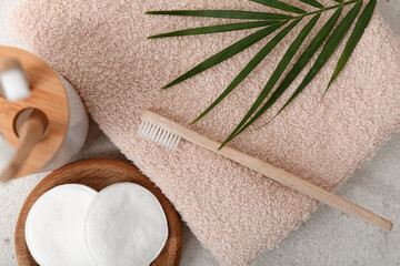 Clean towel, cotton pads, toothbrush and palm leaf on light background, closeup