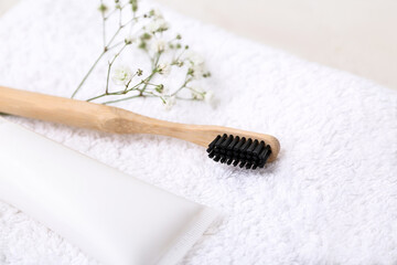 Wooden toothbrush, paste and gypsophila flowers on white towel, closeup