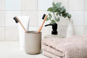 Set of bath supplies with toothbrushes on table against light tile wall