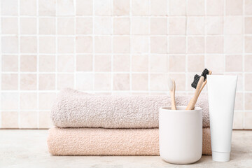 Clean towels, toothbrushes and paste on table against light tile wall