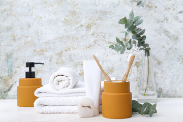 Set of different bath supplies with eucalyptus branches on table against grunge background
