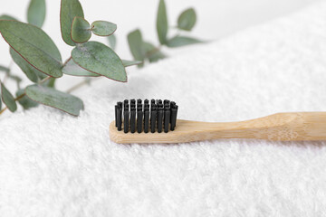 Bamboo toothbrush and eucalyptus branches on light clean towel, closeup