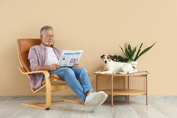 Mature man with cute Jack Russell terrier reading newspaper in armchair at home