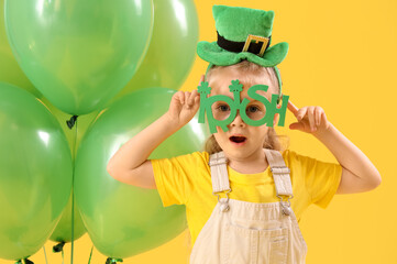 Cute little girl with leprechaun's hat, novelty glasses and balloons on yellow background. St....