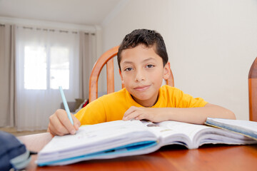 Hispanic boy doing homework at home - boy in yellow t-shirt writing in his notebook - home school - 8 year old boy studying and learning
