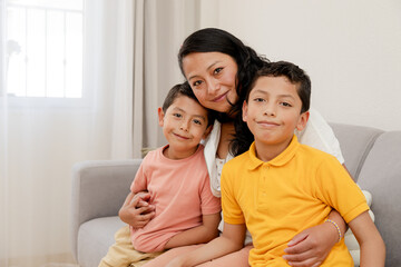 Portrait of mom and children at home-mom hugging hers two children in the living room of her house-single mother with her children-happy little family-Hispanic family