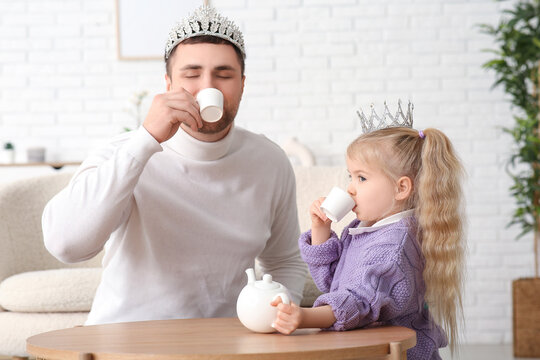 Happy father with his cute little daughter in princess crowns having tea party at home - Powered by Adobe
