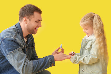 Happy father with his cute little daughter making manicure on yellow background