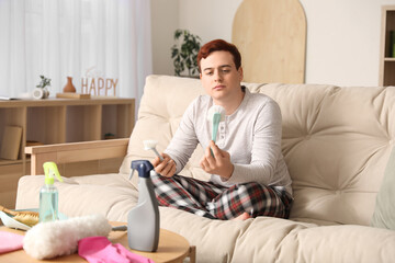 Fototapeta premium Young man holding cleaning brushes on sofa, home chores and domestic responsibilities concept, housekeeping tools