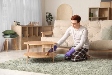 Young man with brush and scoop cleaning table in living room