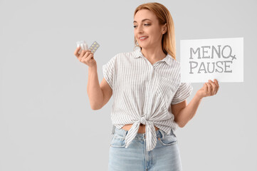 Mature woman holding paper with word MENOPAUSE and pills on light background