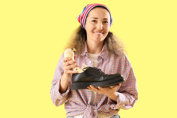 Female shoemaker with wooden shoe tree and boot on yellow background