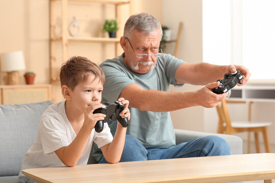 Grandfather with his cute little grandson playing video games at home - Powered by Adobe