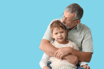 Grandfather kissing his happy cute little grandson hugging on blue background